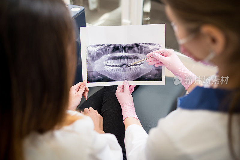 年轻女牙医与女病人在牙科诊所检查x光影像，准备治疗。专注于画面。牙科