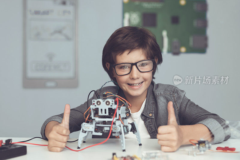 一个戴眼镜的小呆子正抱着一个机器人。男孩看起来很高兴，竖起大拇指