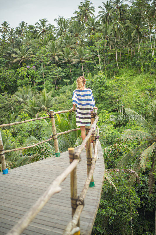 年轻女子在丛林上方的木制露台上凝视着大自然的美丽