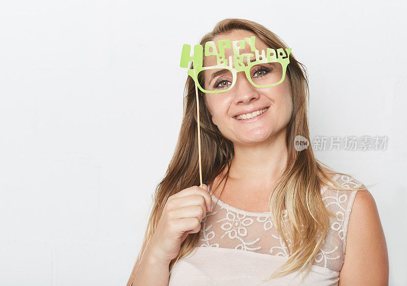 漂亮的金发女郎微笑着，拿着“生日快乐”的照相亭眼镜