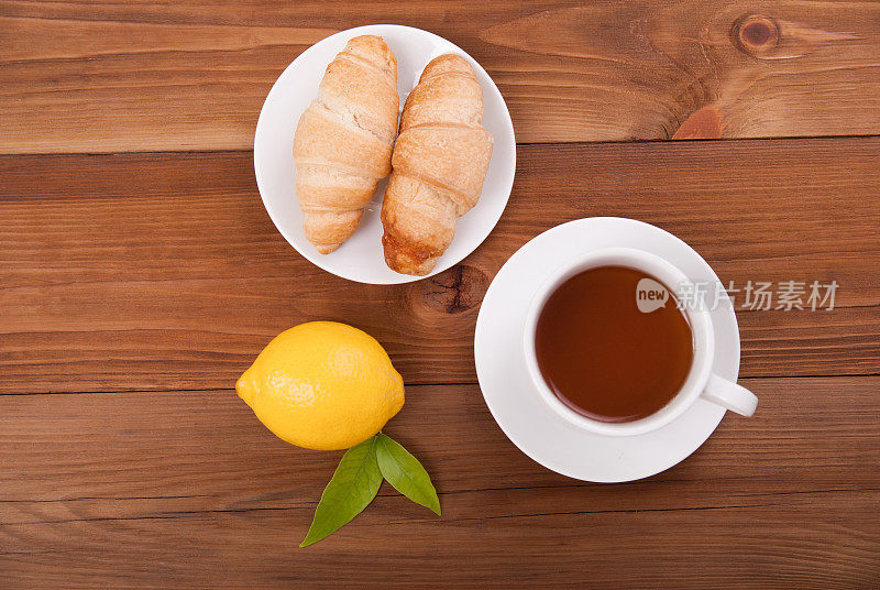 一杯茶，柠檬和羊角面包，木质背景。