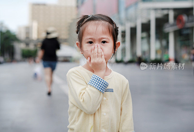 一个亚洲小女孩用手捂住自己的嘴和鼻子。