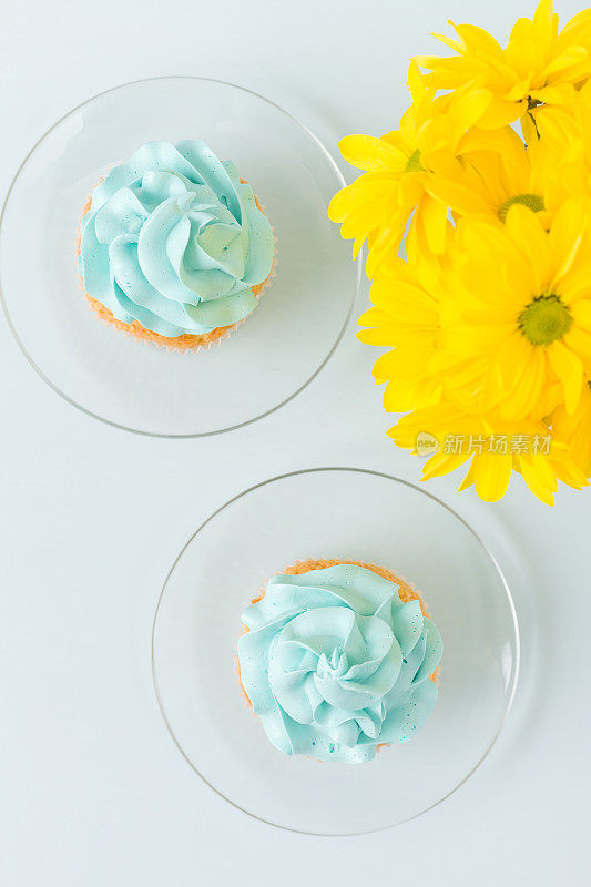杯形蛋糕上有甜蓝奶油装饰，杯中有一束黄色菊花。Flat-lay概念