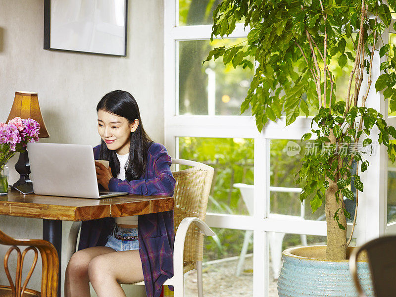 年轻的亚洲女人在咖啡店里使用笔记本电脑