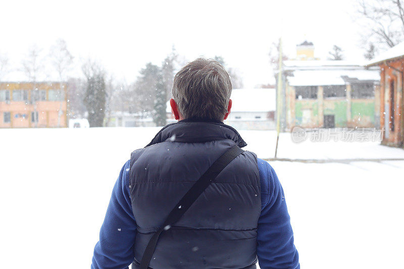 一个白发苍苍的成年男子在大雪纷飞的冬天走在城市里