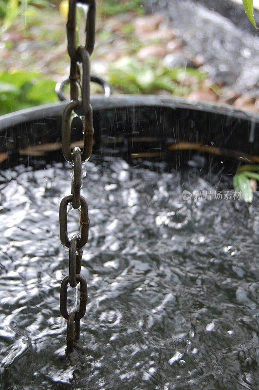 雨水溅进有水的浴缸里，雨水顺着一条链流下来。