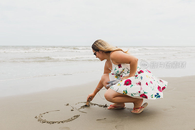 年轻女子在沙滩上的沙子上写字