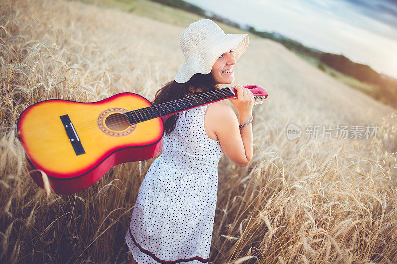 一个女人和浪漫的走过麦田，背后有一把吉他。