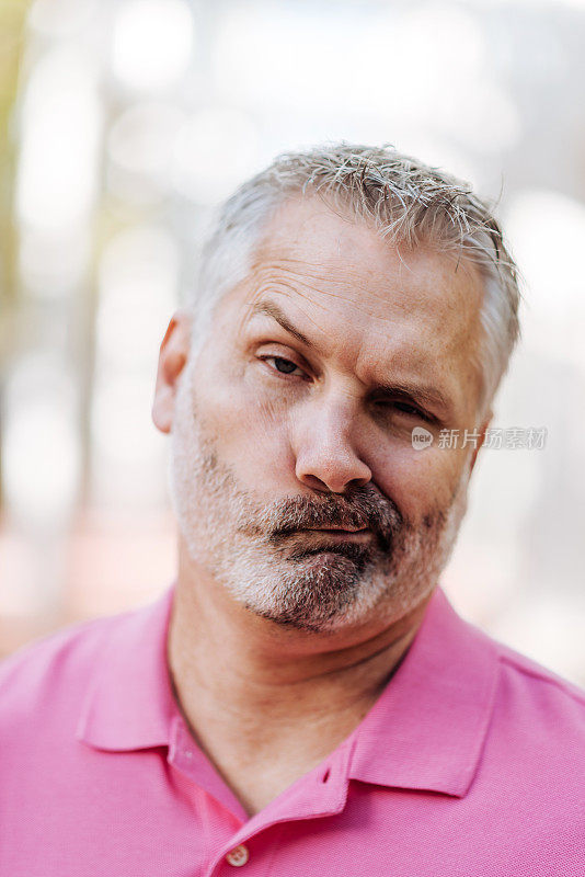 成年白人男子的肖像与灰色头发在粉红色polo衫与有趣的面部表情
