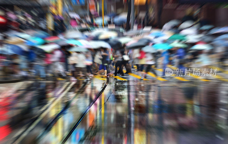 动作模糊的行人在雨中穿过香港街道，反射出来