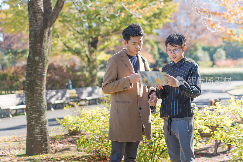 年轻的亚洲男子和日本朋友寻找旅游地点使用手机和花时间在亚洲旅行