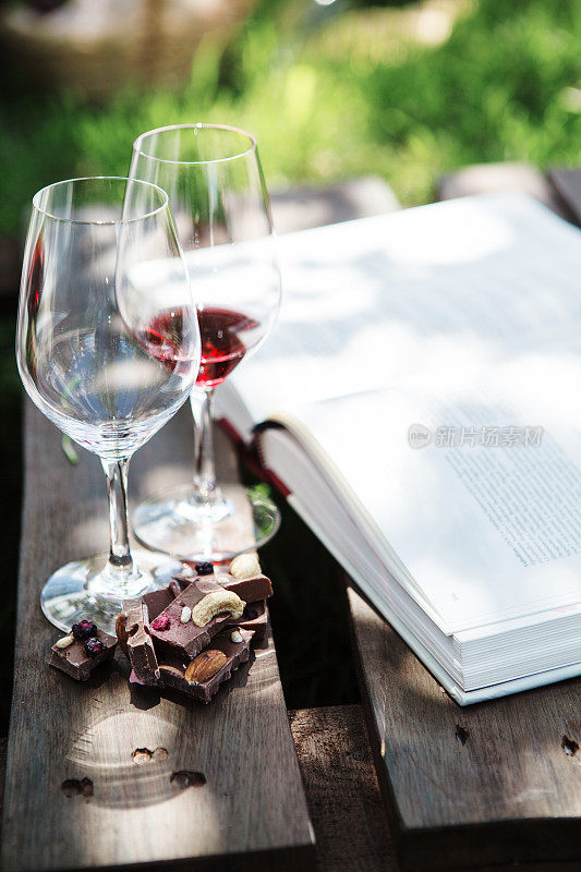 杯子里放着红葡萄酒和白葡萄酒，几块巧克力，一本书