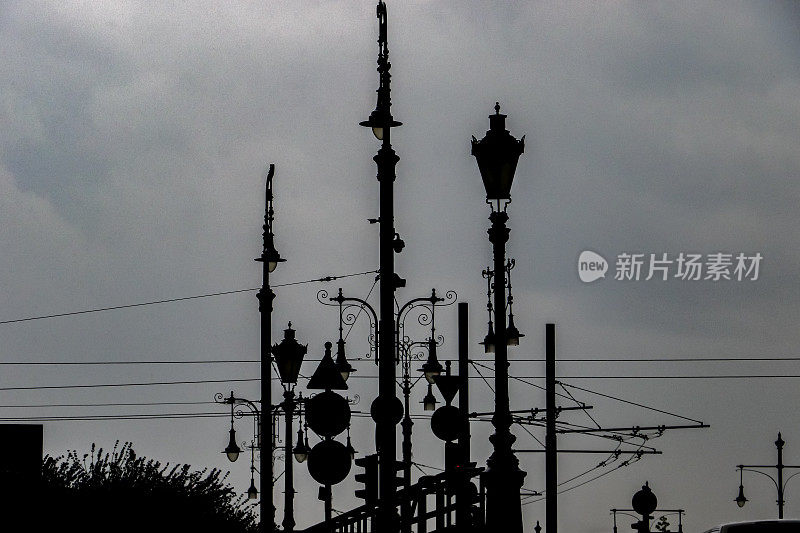 维多利亚风格的煤气灯、现代路标、架空电线和有轨电车缆线在暴风雨云的背景下形成剪影