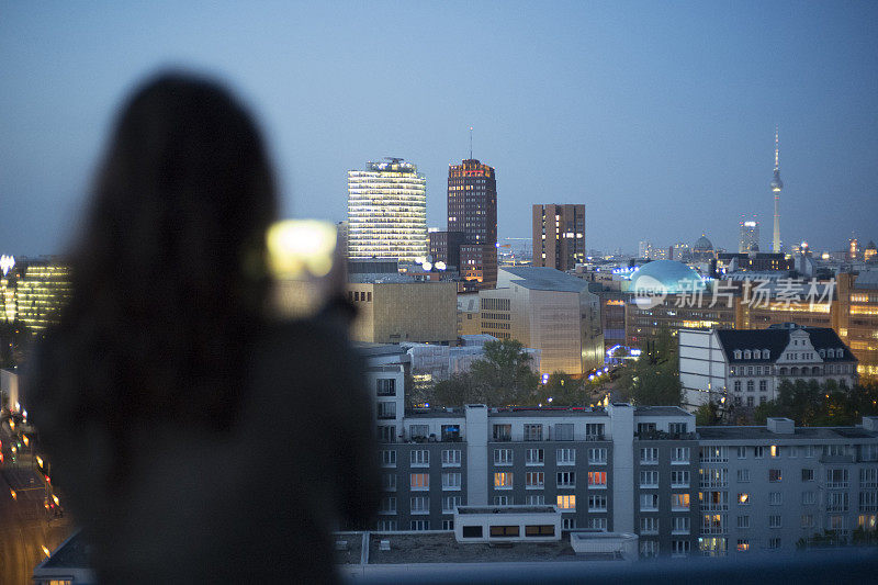 一个年轻的女人用手机拍摄柏林的天际线的后视图