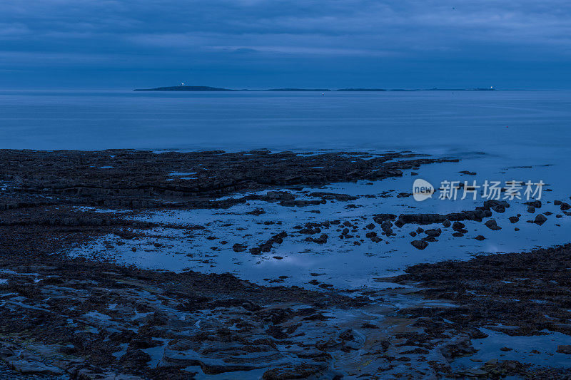 在英国诺森伯兰郡海岸，雾气蒙蒙的法恩群岛在地平线上的低潮时，数码增强的傍晚拍摄。