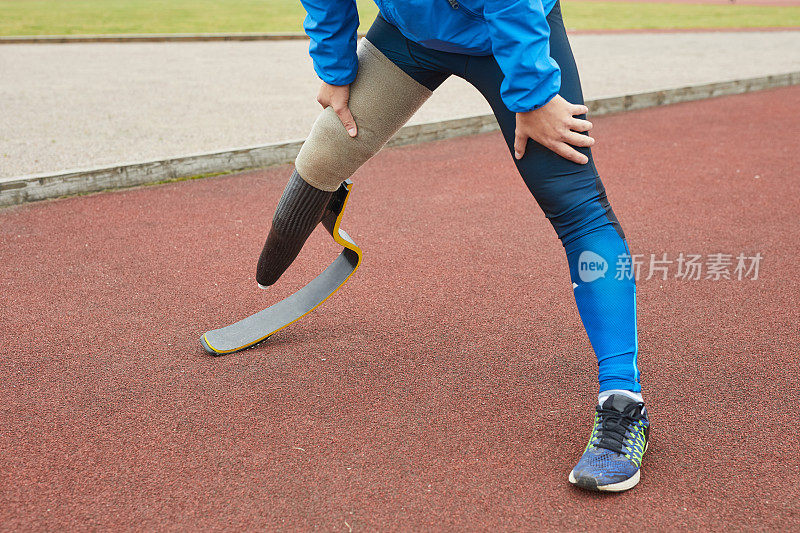 特写镜头，一个不认识的截肢男子在蓝色运动紧身裤站在体育场和伸展腿之前跑步