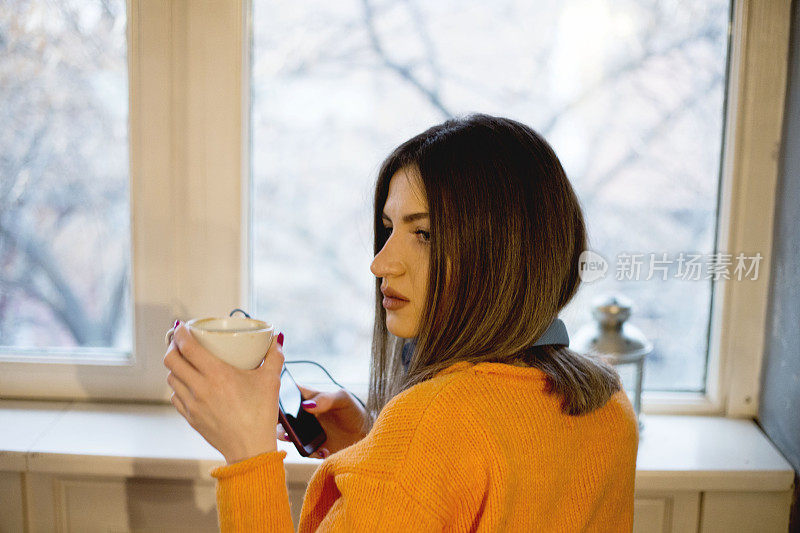 美丽的年轻女子，早上在窗边喝咖啡