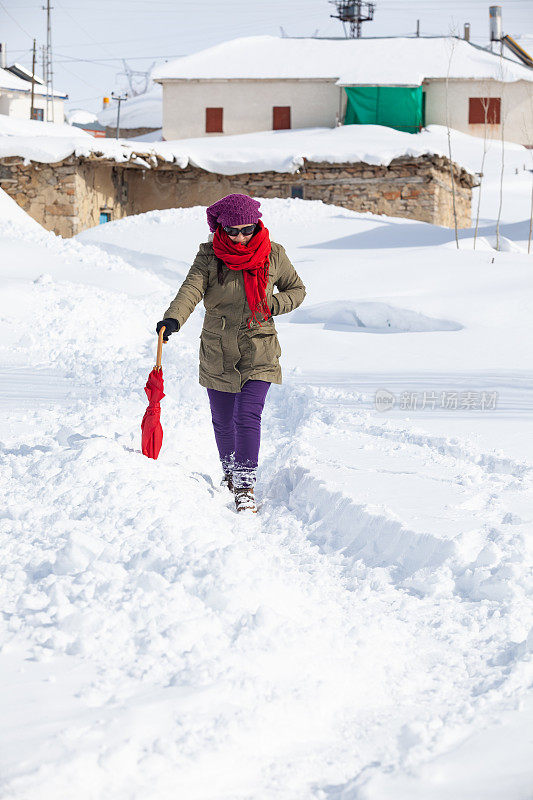 成年妇女穿着暖和的衣服在雪地上行走在农村