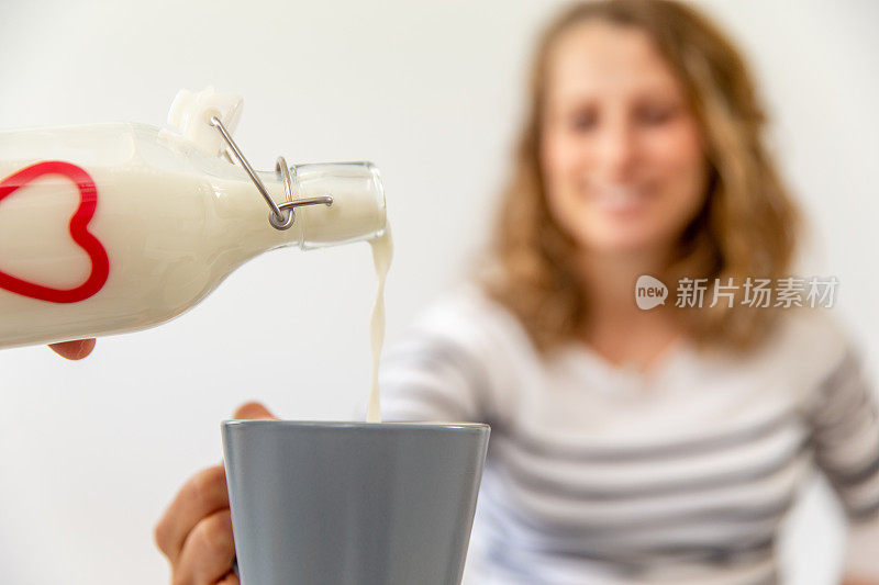 有机牛奶的特写从瓶子倒进马克杯由年轻微笑的女人-库存照片