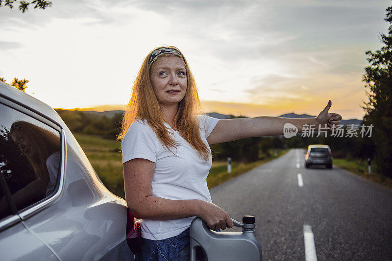 一位妇女在路上试图修理一辆坏了的汽车。这位妇女给她的车加油，试图继续旅程。一个女人带着一桶汽油在一辆车旁边