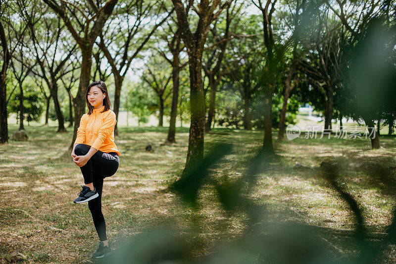 运动的亚洲华人妇女伸展她的腿和做热身运动