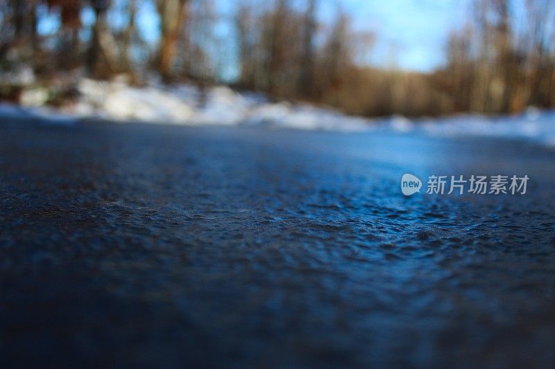 森林里结冰的蓝色水坑。在结冰的水池后面是一片森林。背景是树。冬天。冷。