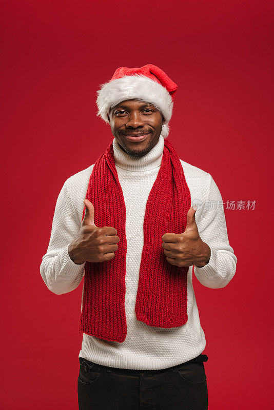 一个年轻的黑人穿着羊毛衫，戴着圣诞帽，微笑着竖起双手的大拇指