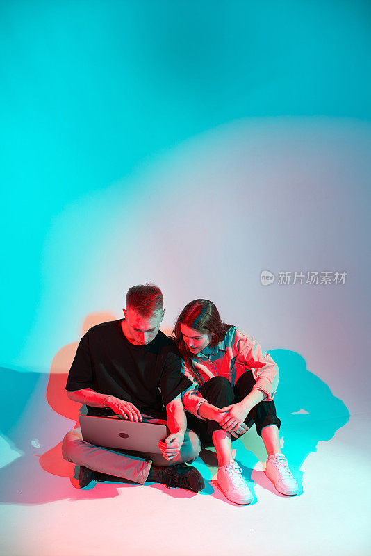 酷时尚的年轻夫妇与笔记本电脑。彩色的霓虹灯。为社交网络写博客的男孩女孩
