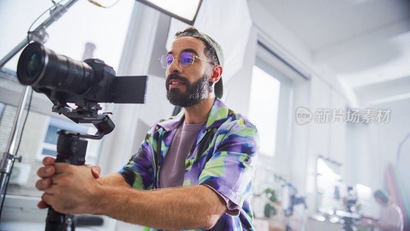 有胡子的男摄影师，穿着彩色衬衫，在明亮的工作室里操作专业摄像机，为电影或广告项目捕捉引人入胜的内容。