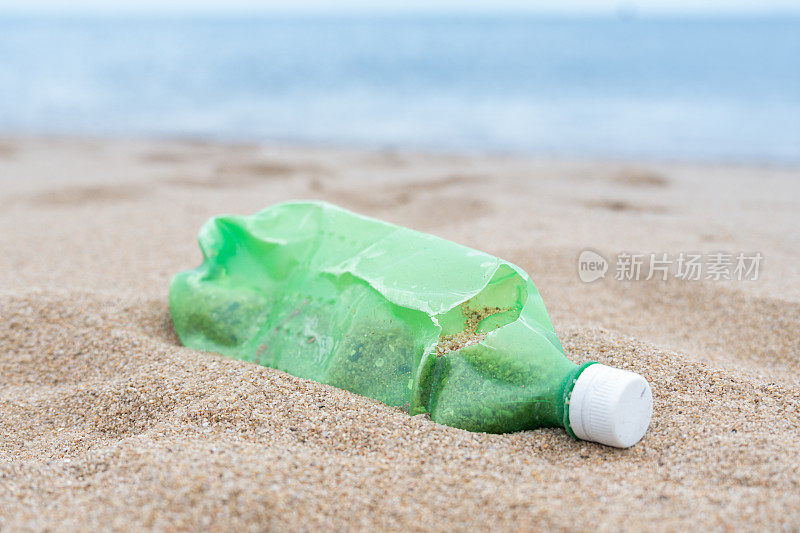 一个绿色的塑料瓶躺在沙滩上的特写镜头，显示了塑料污染污染了环境，表明了海岸清理和保护的必要性。