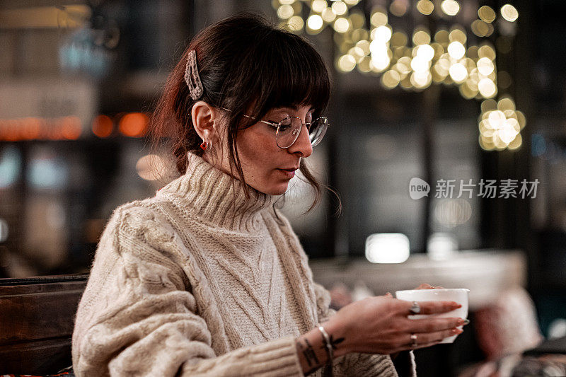在餐馆里喝咖啡的女人。她穿着一件高领毛衣，戴着一副眼镜