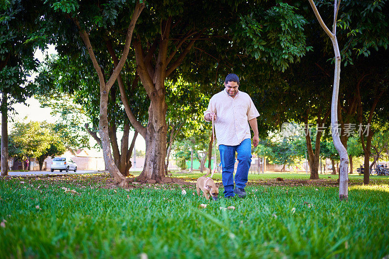 一个拉丁男人带着他的狗在公园里散步