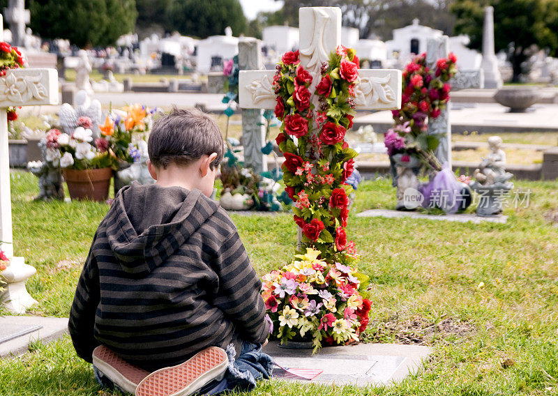 小男孩跪在坟墓前哀悼