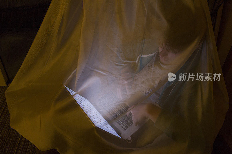 年轻人在蚊帐下使用笔记本电脑