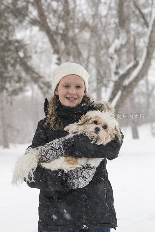 女孩抱着她的小白狗在冬天的暴风雪