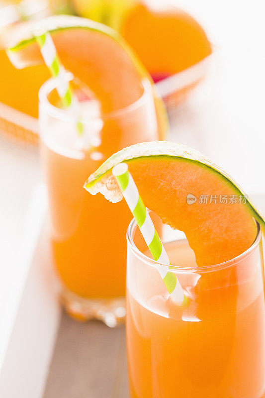 新鲜的甜瓜汁装在玻璃杯中，用吸管饮用