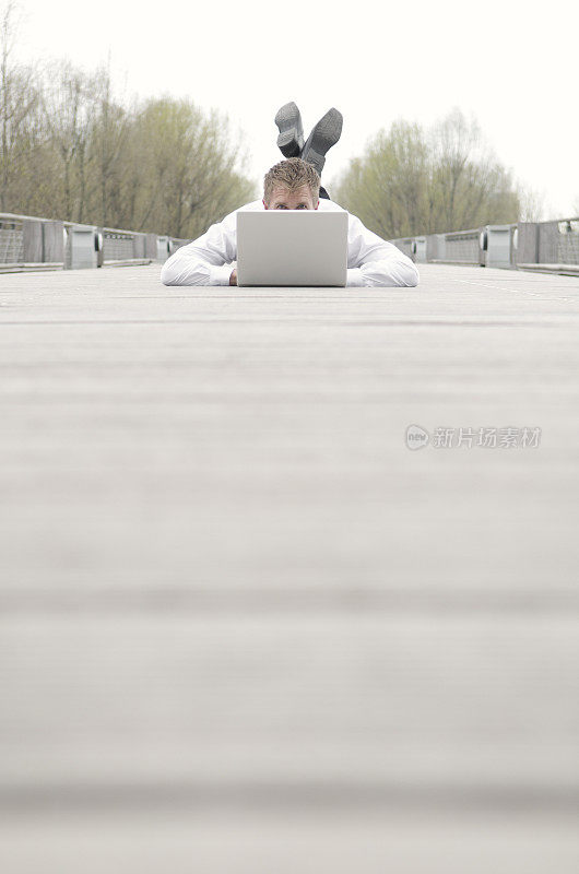 一个带着笔记本电脑躺在木板路上的家伙