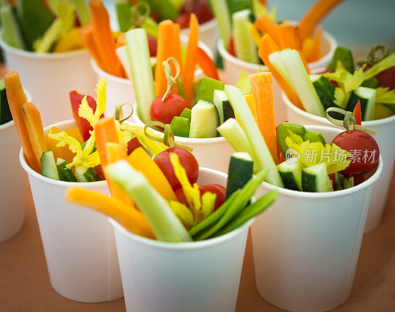 健康生胡萝卜、黄瓜、辣椒棒和樱桃番茄装在纸玻璃杯里放在桌上