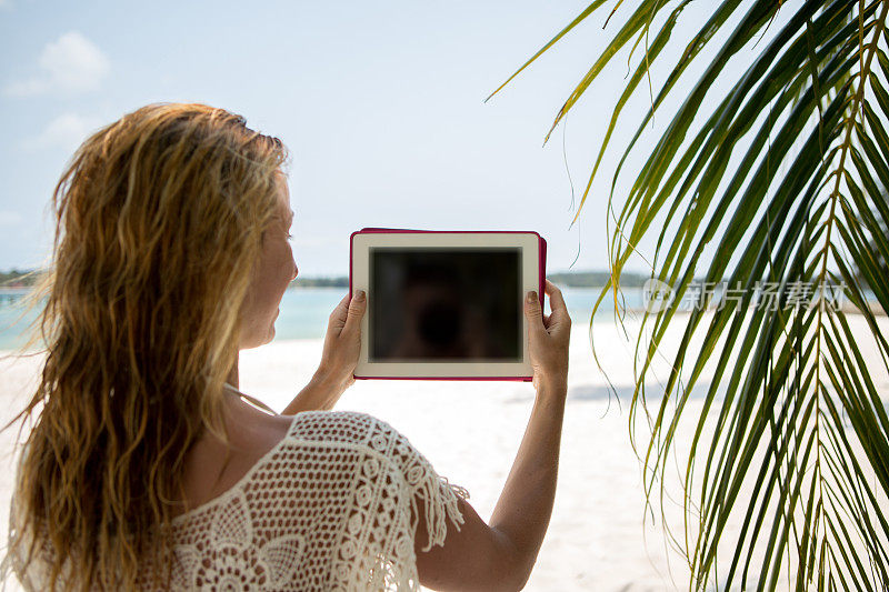一名女子在热带海滩上用平板电脑拍照
