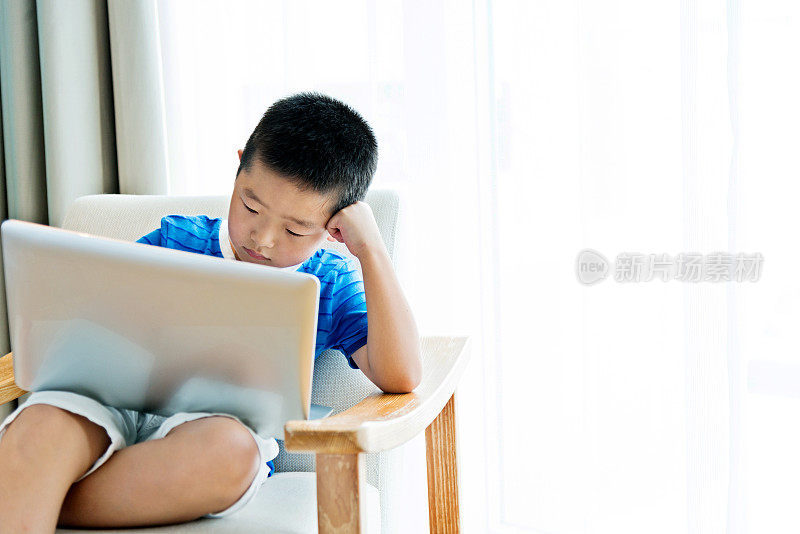 小男孩坐在扶手椅上用笔记本电脑