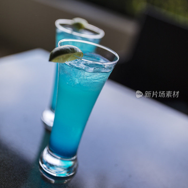 在巴拿马城的露台上，两款清爽的蓝色飓风鸡尾酒由朗姆酒、库拉索酒、橙汁和菠萝汁调制，配上青柠角和大量冰块。