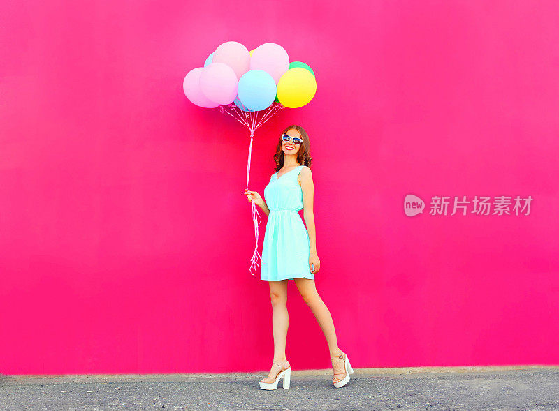 快乐微笑的女人与一个空气彩色气球走过一个粉红色的背景