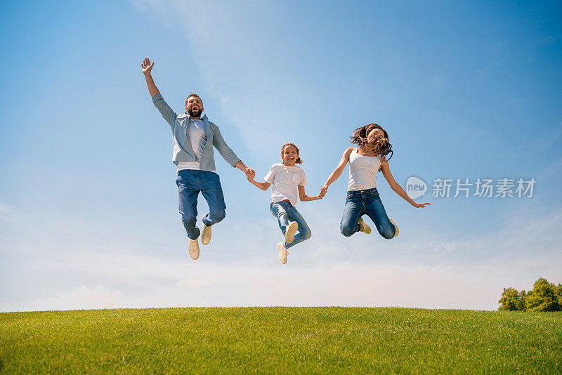 幸福的年轻家庭和一个孩子手牵着手，在草地上跳跃