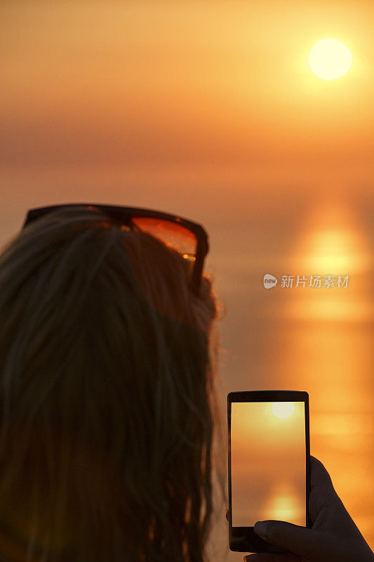 女人用智能手机在日落的地中海渔船拍照