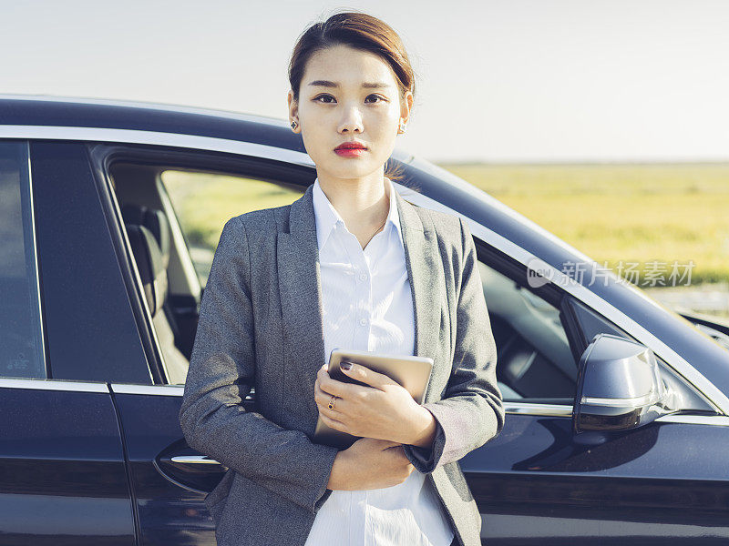 亚洲女商人手持平板电脑站在汽车旁的肖像