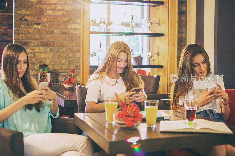 三个十几岁的女孩在咖啡馆使用智能手机。