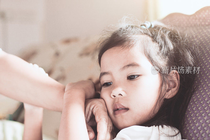 可爱的亚洲女孩生病和母亲的手摸她的脸来检查温度