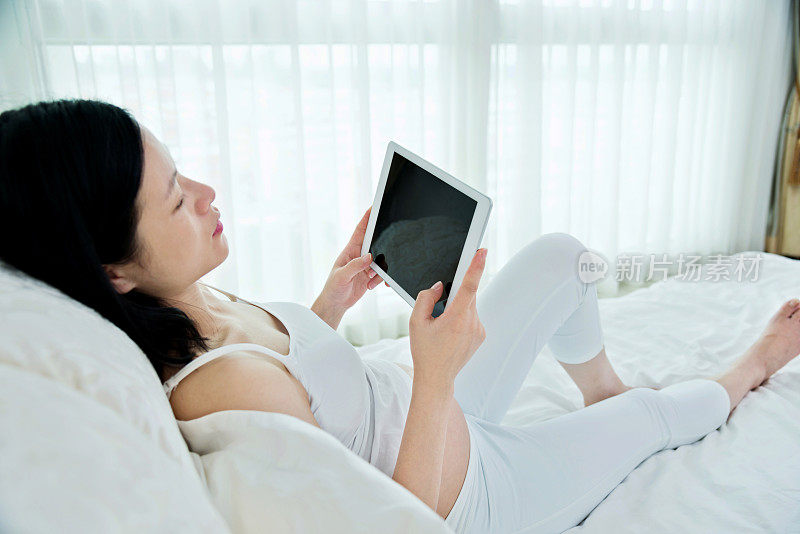 孕妇在床上使用平板电脑