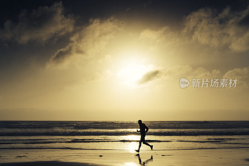 一个人的剪影沿着海滩跑在日落附近。