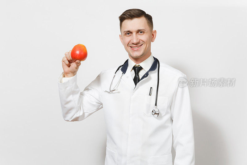 微笑英俊的年轻医生男子孤立在白色的背景。男医生在医疗制服听诊器拿着红苹果。医护人员健康医学理念。适当的营养。本空间